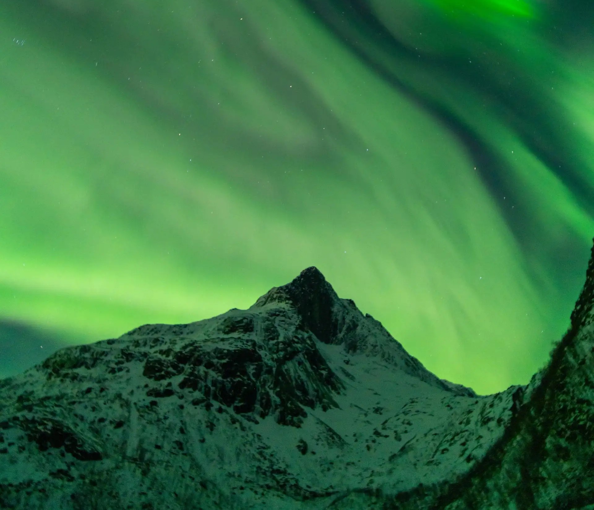 Grønne nordlys som strømmer over en snødekt arktisk fjelltopp ved Tromsø